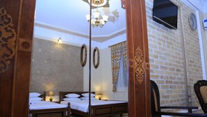 A hotel room with two wooden beds, a chandelier, patterned walls, and a brick wall. - Grand Emir Residence (Bukhara)