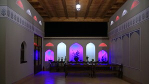 A room with a wooden ceiling, arched windows with decorative patterns, and a central area with a bench and vases. - Grand Emir Residence (Bukhara)