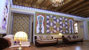 A traditional interior with wooden beams, a chandelier, patterned wall decorations, and two sofas. - Grand Emir Residence (Bukhara)