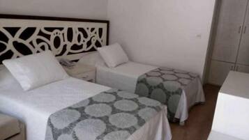 Habitación sencilla y limpia con dos camas individuales, una mesita de noche y un armario.