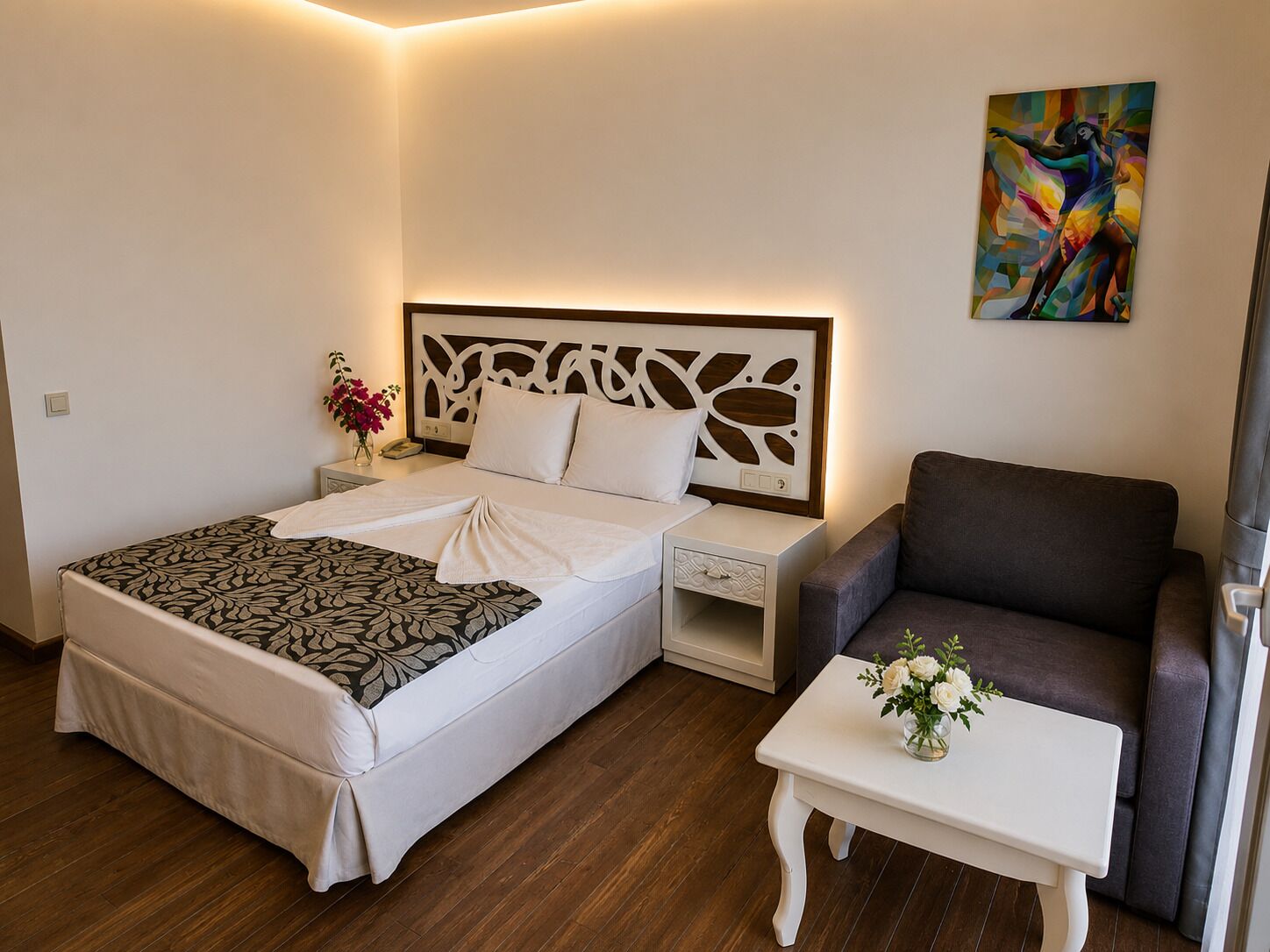 A hotel room with a bed, bedside table, chair, and a painting on the wall.