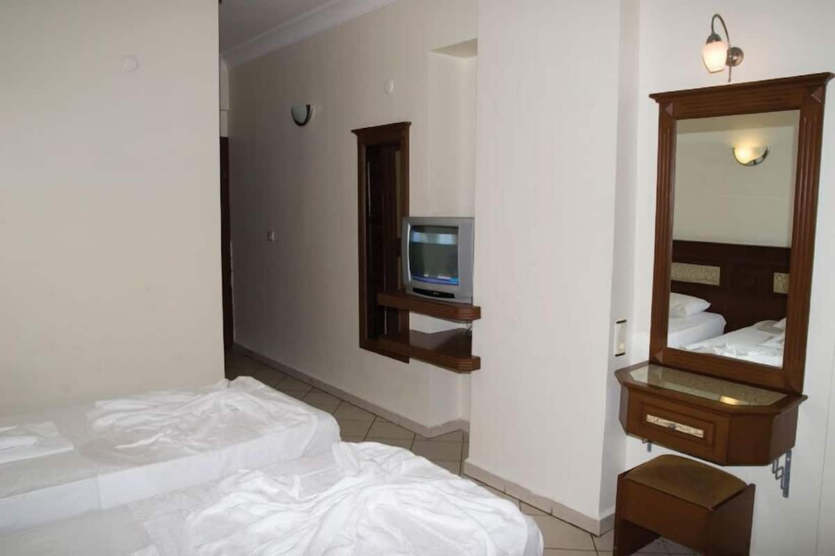 A hotel room with a bed, a small TV on a shelf, a mirror, and a wooden bench.