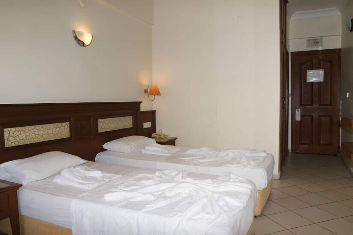 A hotel room with two beds, a nightstand, a wall-mounted lamp, and a door with a sign.
