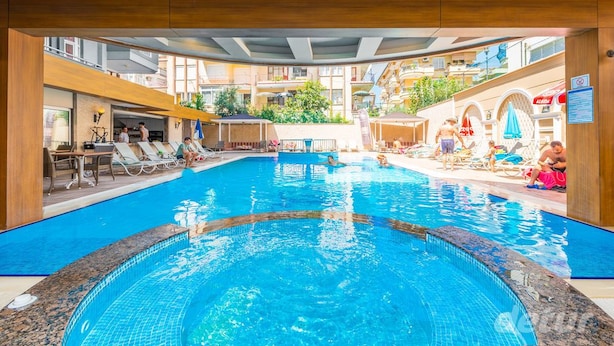 A swimming pool with lounge chairs and umbrellas, surrounded by a wooden deck and buildings. - Lavinia Apart Hotel (Alanya)