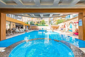 A swimming pool with lounge chairs and umbrellas, surrounded by a wooden deck and buildings.
