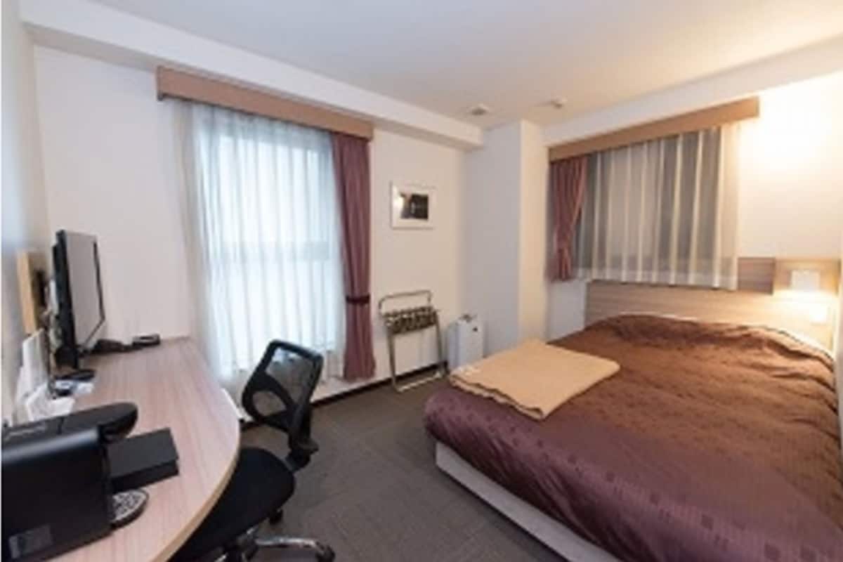 Una camera d'albergo con un letto, una scrivania con un computer, una sedia e una finestra con tende.