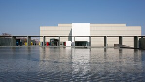 A modern building with a flat roof and a large open plaza in front. - Toyota Prestige Hotel (Toyota)