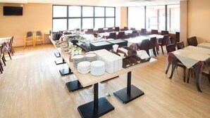 A large dining area with multiple tables and chairs, a buffet setup with plates and bowls, and a large window providing natural light. - Toyota Prestige Hotel (Toyota)