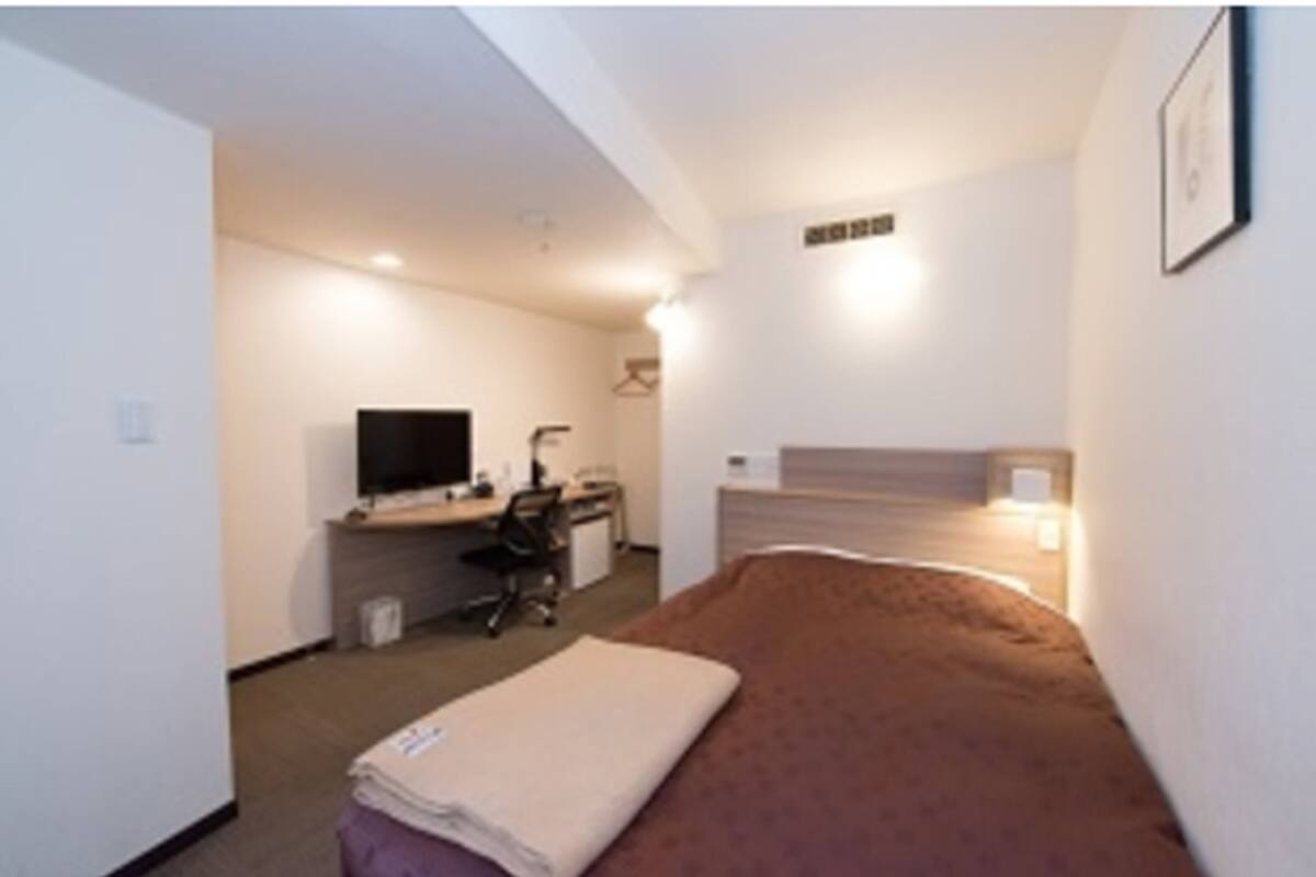 Una camera d'albergo funzionale con un letto, una scrivania, una sedia, una televisione e un piccolo angolo studio.