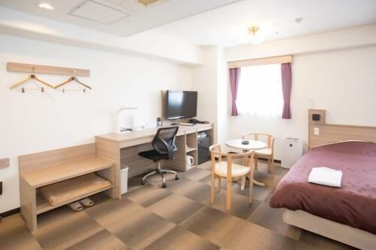 Una camera d'albergo con un letto, una scrivania, una sedia, una televisione e un tavolino.