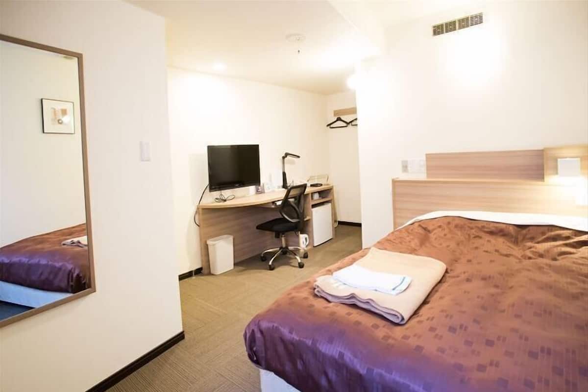 Una camera d'albergo con un letto, una scrivania con un computer, una sedia e una televisione.
