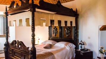 Una cama con dosel y tallas ornamentales, una mesita de noche con lámpara y un espejo en la pared.