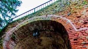 Un sendero de piedra bajo un arco de ladrillo que conduce a un edificio con fachada blanca y una ventana pequeña.