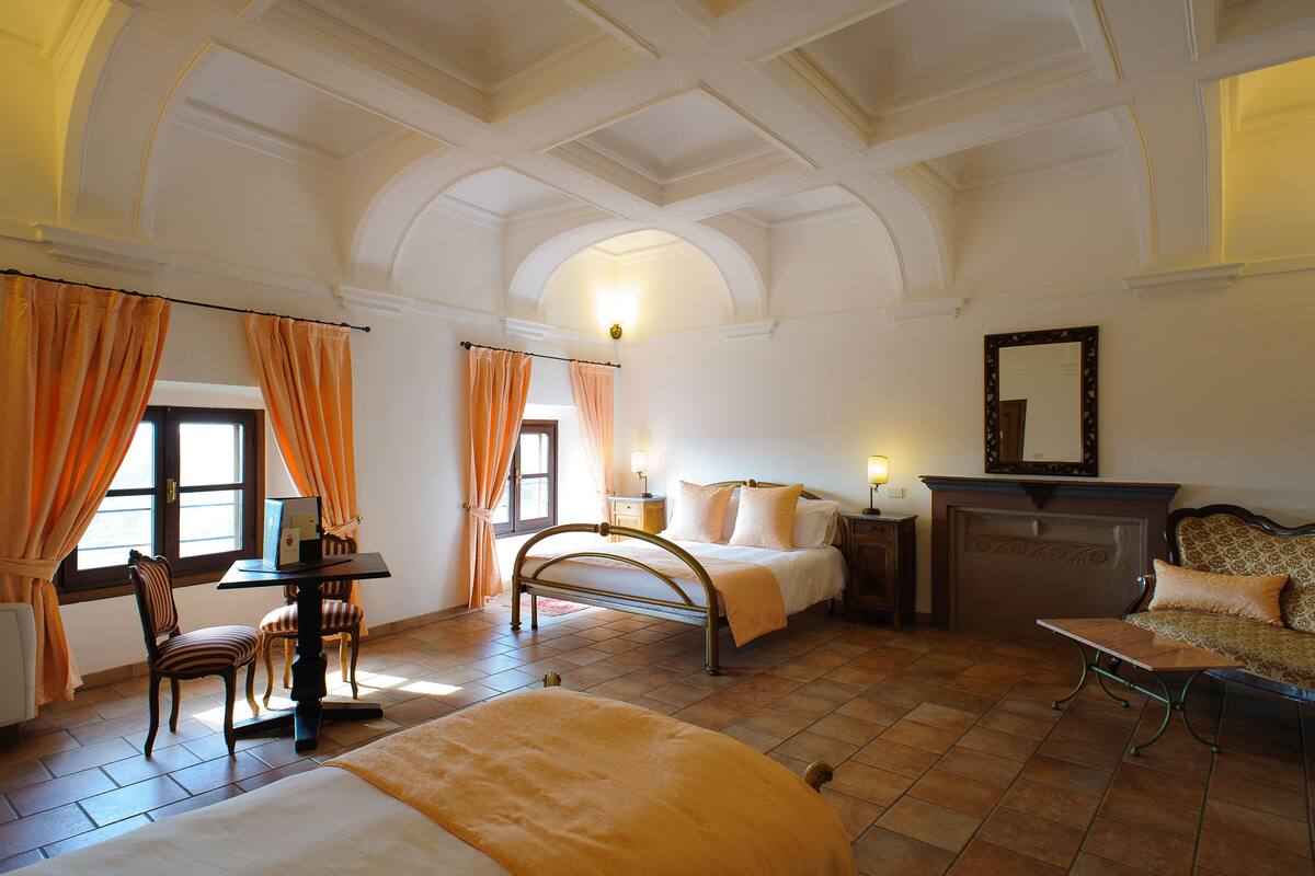 A hotel room with a bed, a desk, a chair, a fireplace, and a mirror on the wall.