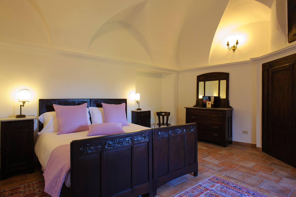 A bedroom with a large bed, two bedside tables, a dresser, a mirror, and a patterned rug.