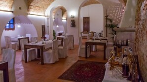 Un comedor con varias mesas dispuestas para una comida, con sillas blancas y una mesa central adornada con un centro de mesa decorativo.