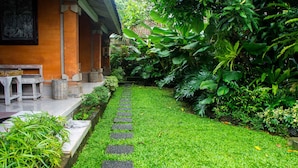 A garden pathway with stepping stones, surrounded by lush greenery and a traditional building with a tiled roof. - Bale Bali Inn (Ubud)