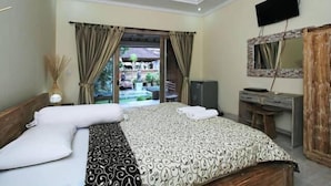 A bedroom with a large bed, a desk, a television, and a view of the outside. - Bale Bali Inn (Ubud)