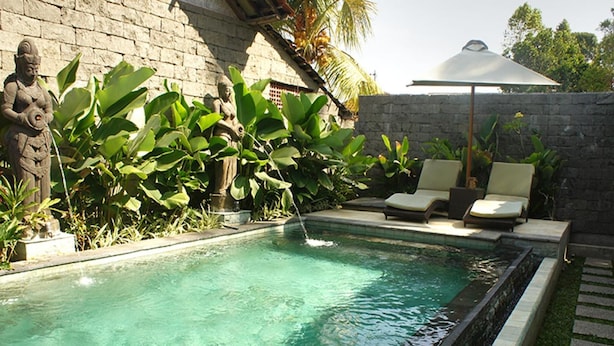A swimming pool with a stone wall and tropical plants. There are lounge chairs and a sun umbrella. - Bale Bali Inn (Ubud)