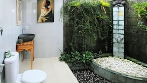 A bathroom with a toilet, sink, and a wall-mounted painting. - Bale Bali Inn (Ubud)