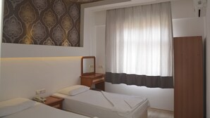 Hotellihuone, jossa on kaksi sänkyä, puinen työpöytä, peili ja ikkuna, jossa on verhot.