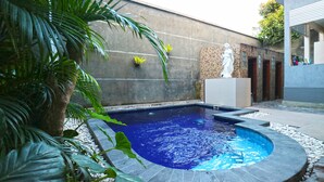 A swimming pool with a stone border, surrounded by plants and a statue. - DD Living - Hostel (Tibubeneng)