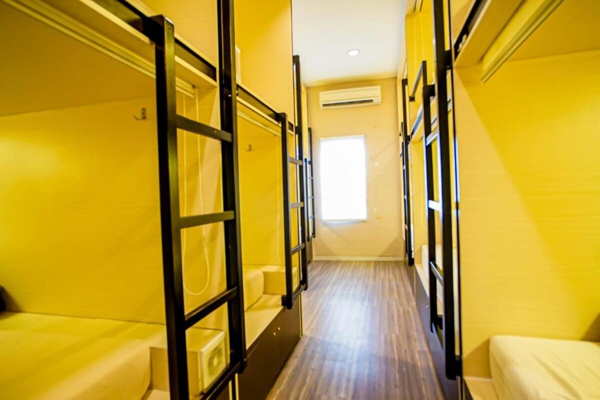 A narrow corridor with bunk beds on either side, a window at the end, and a wooden floor.