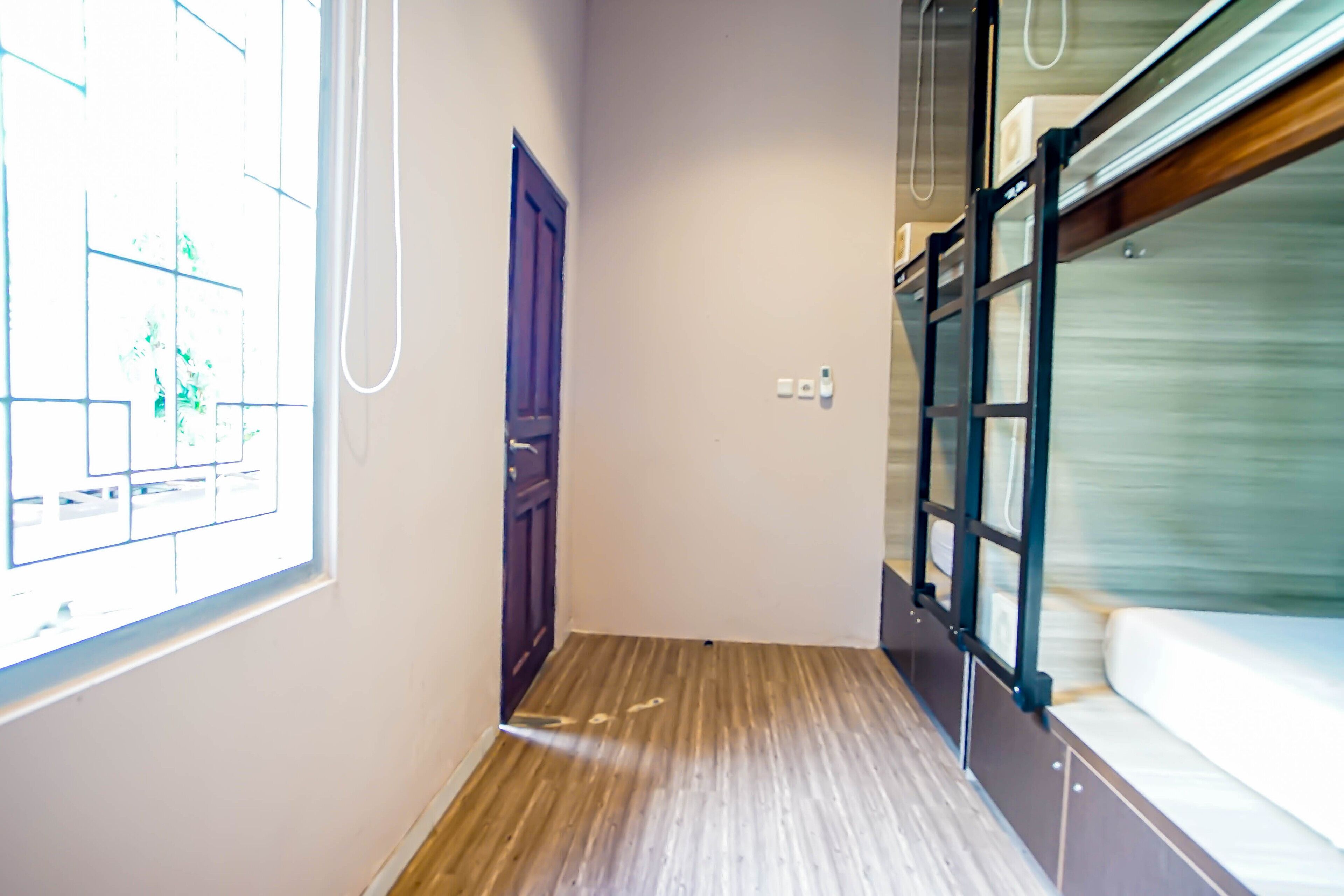 Un estrecho pasillo con suelo de madera, una ventana con persianas, una puerta y una cama litera con colchón.