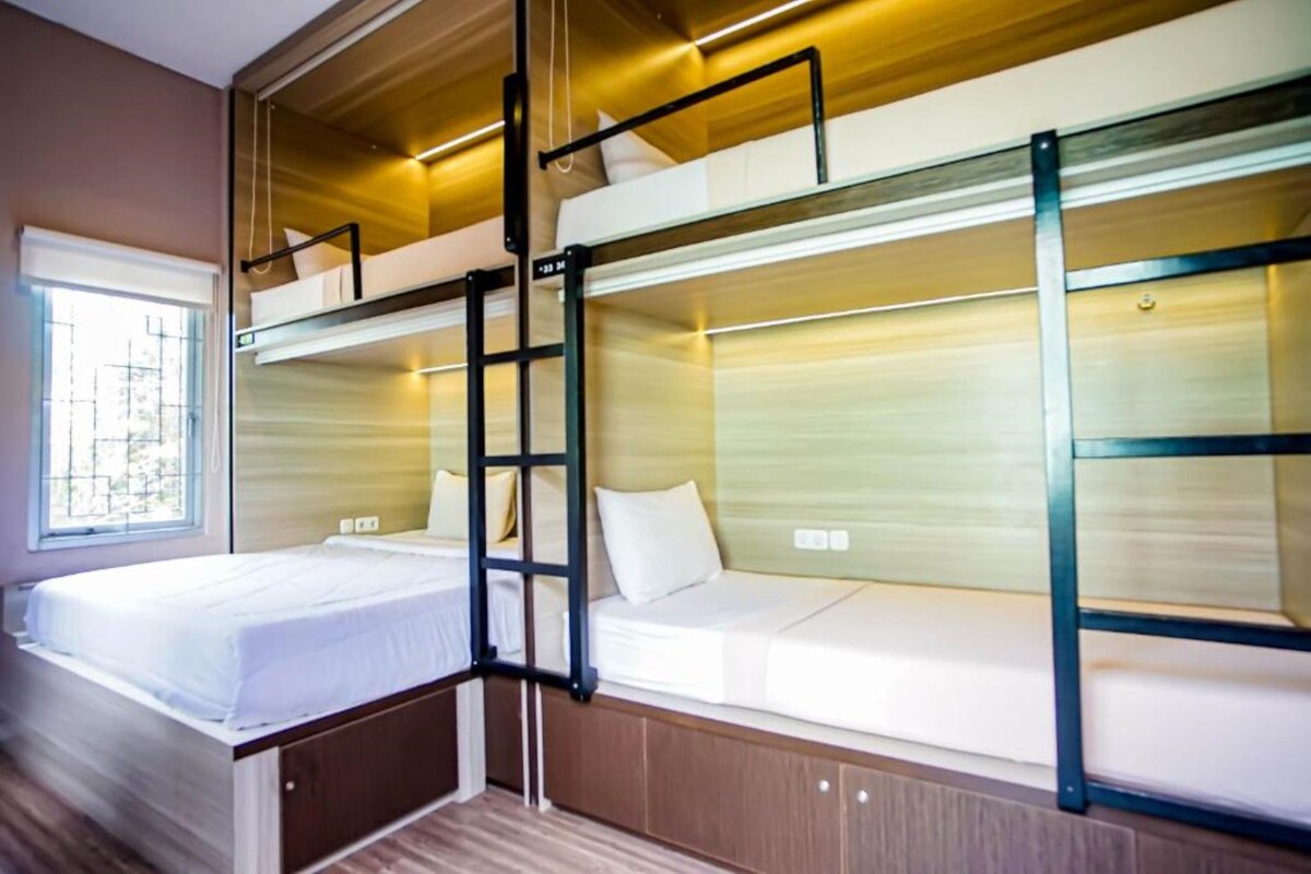 A bunk bed room with a ladder, wooden flooring, and a window with blinds.