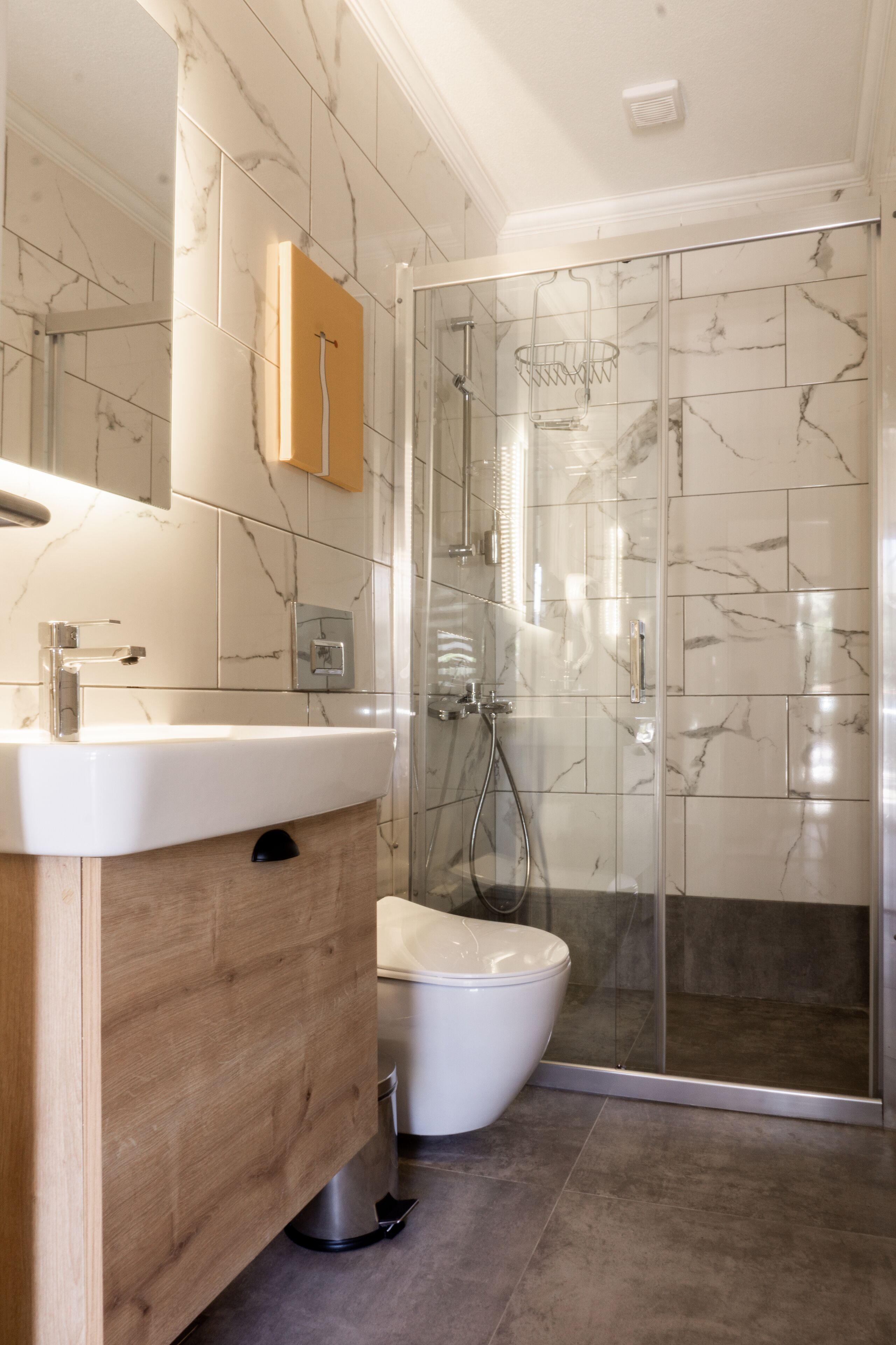 A modern bathroom with a marble-tiled shower enclosure, a wooden vanity, and a white sink.