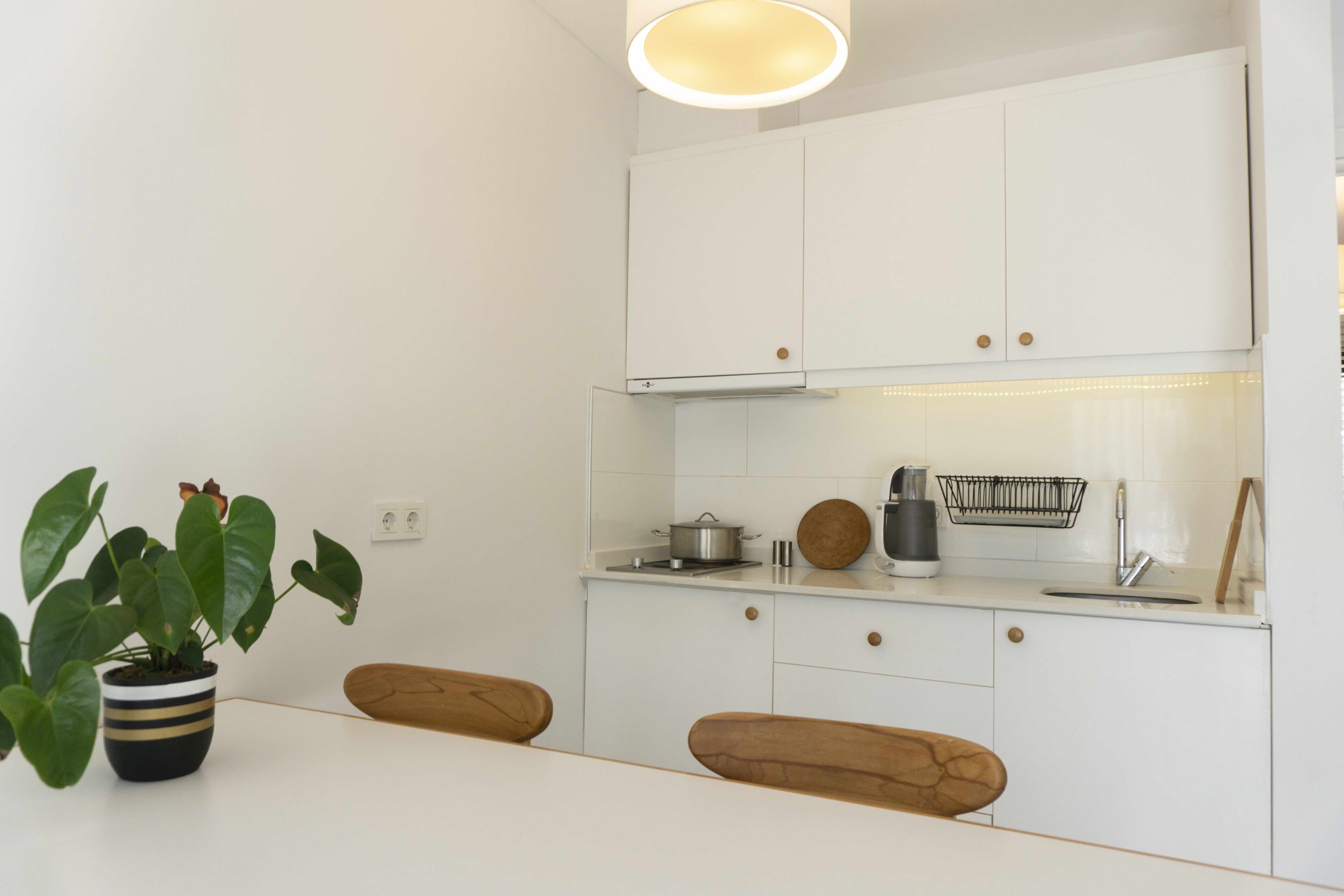Een moderne keuken met witte kastjes, een houten eettafel en een plant in een pot.