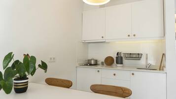 Een moderne keuken met witte kastjes, een houten eettafel en een plant in een pot.