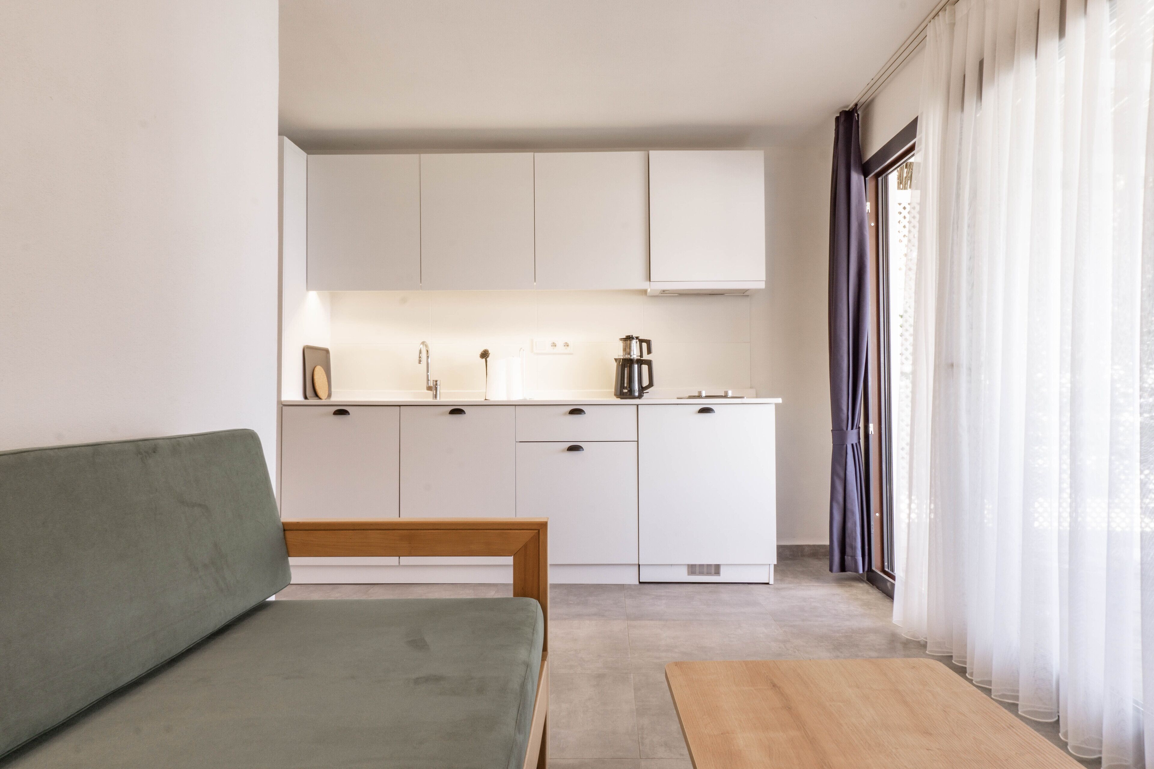 A minimalist kitchenette with white cabinets, a wooden bench, and a table.