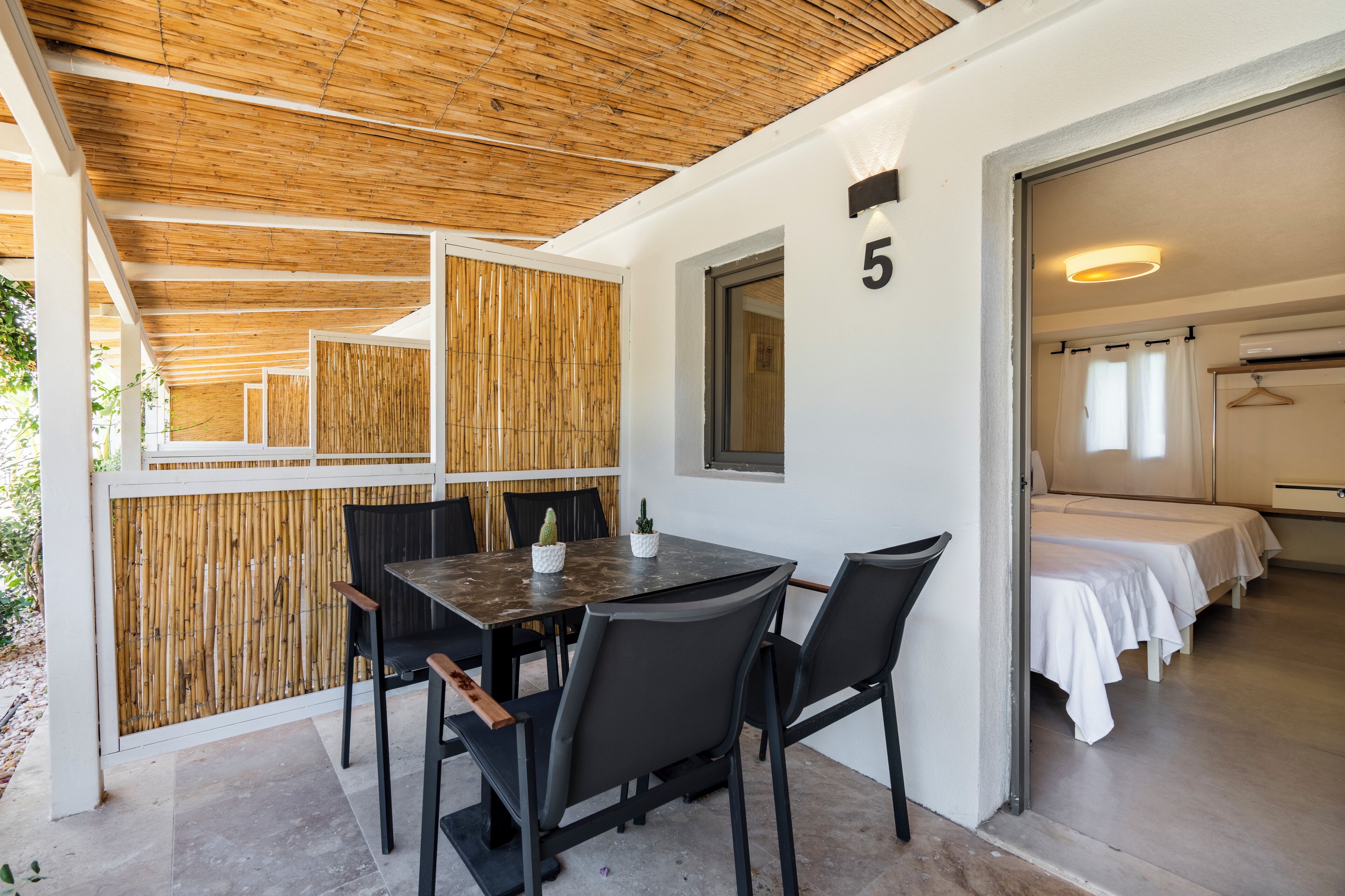A room with a wooden ceiling, a table with chairs, and a bed with white linens.