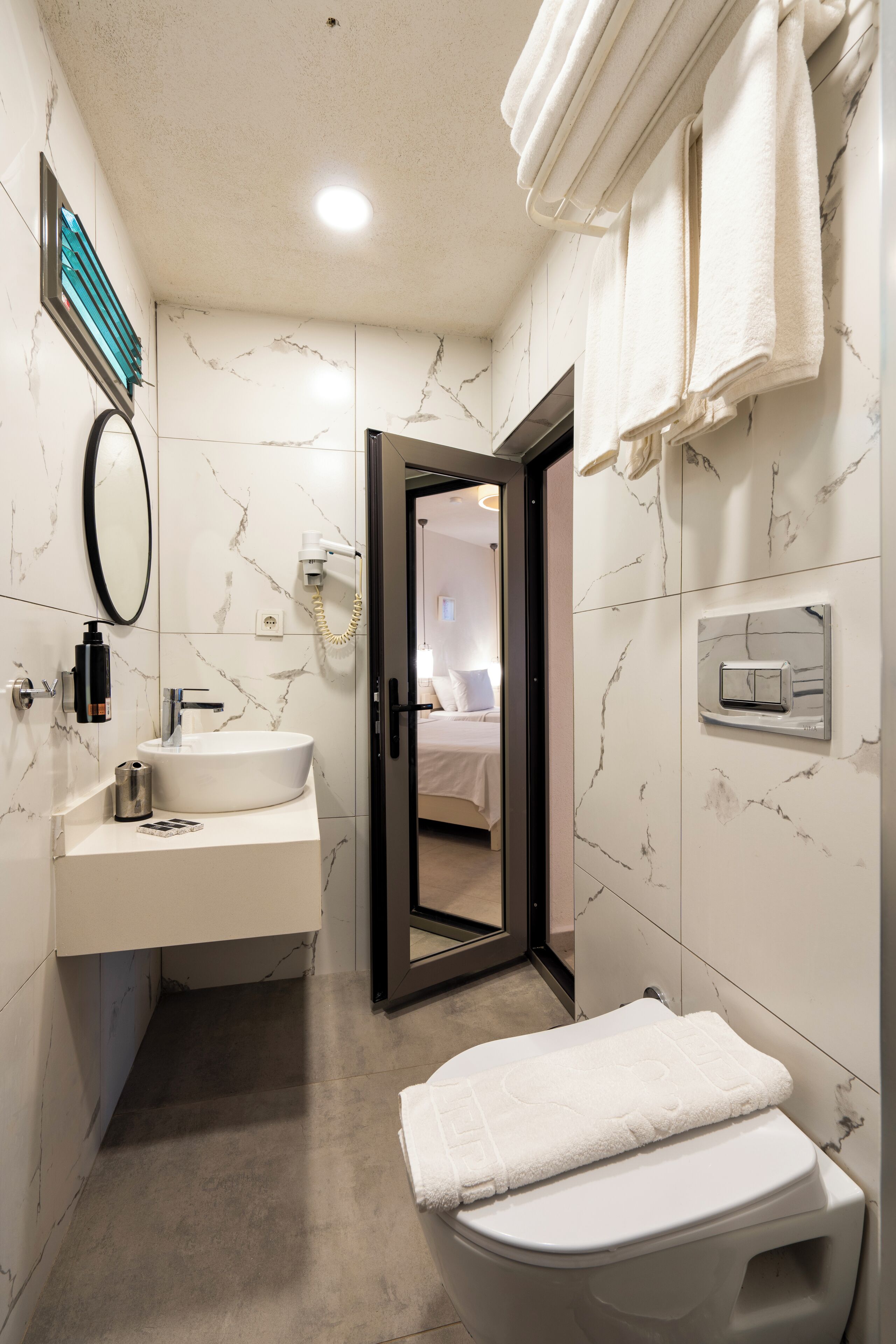 A modern bathroom with a marble backsplash, a built-in sink, a toilet, and a mirror.