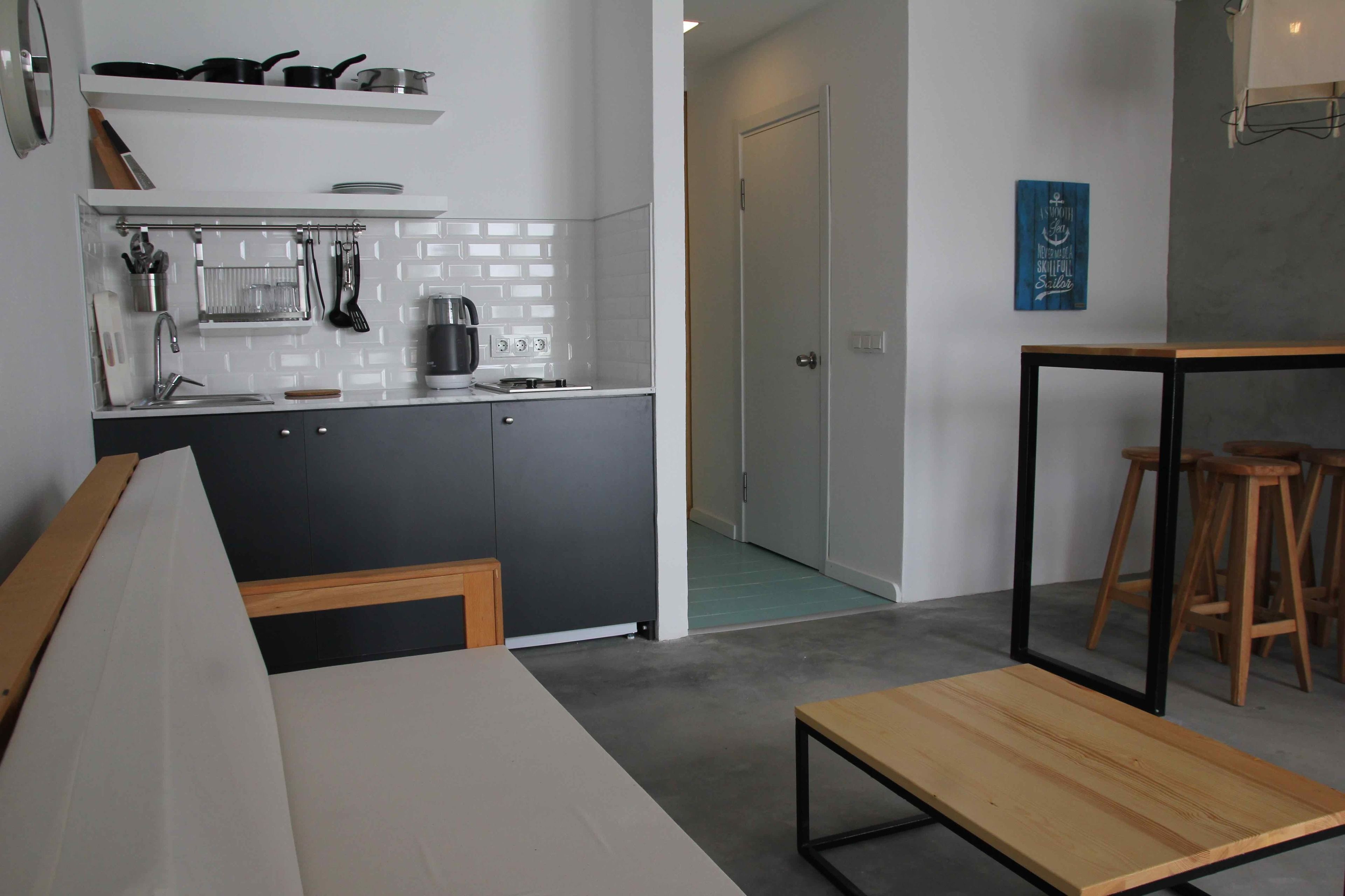 A modern kitchen with a white countertop, black cabinets, and a wooden table. There is a door leading to another room and a blue sign on the wall.