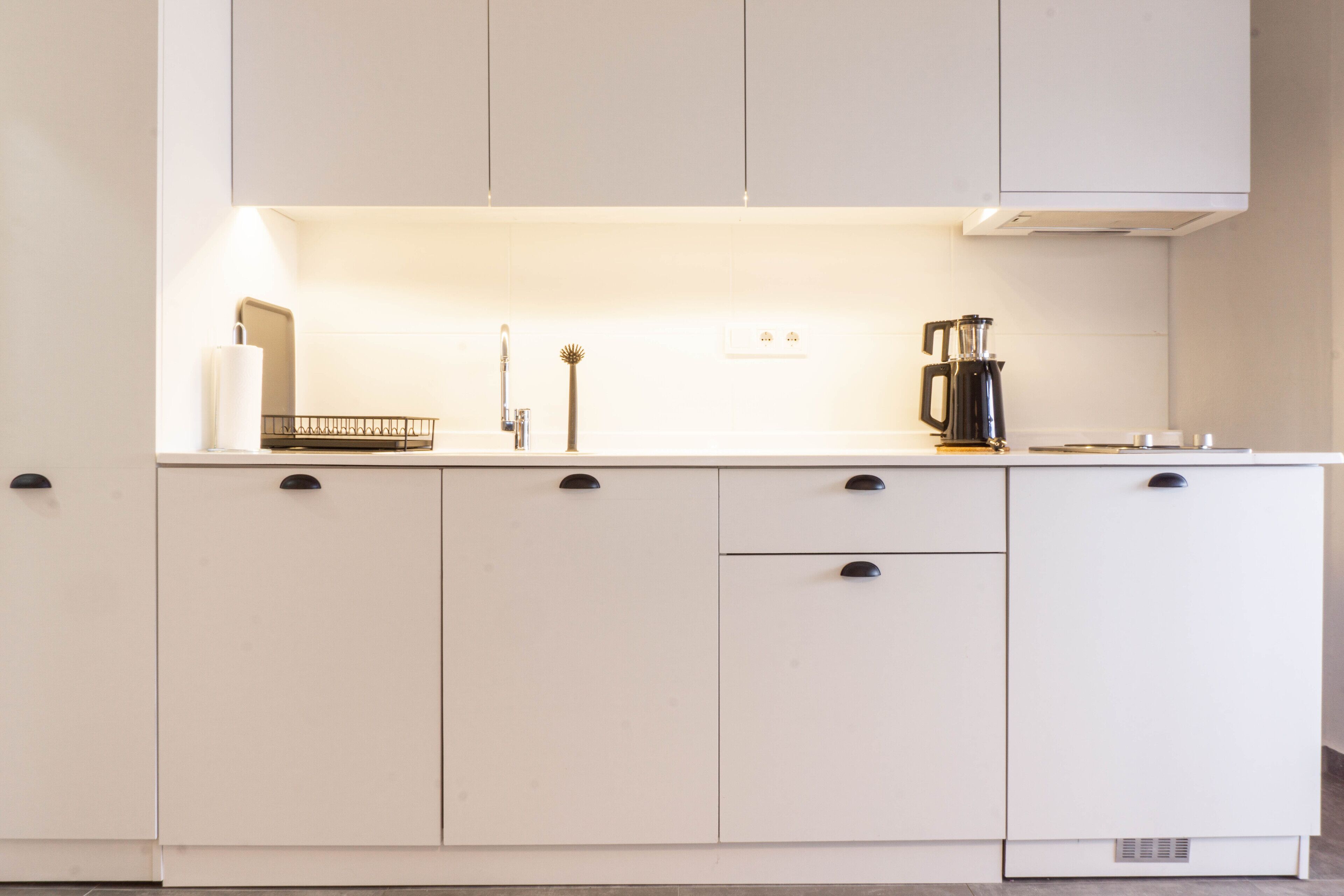 Una cocina con armarios blancos, una cafetera y un hervidor.