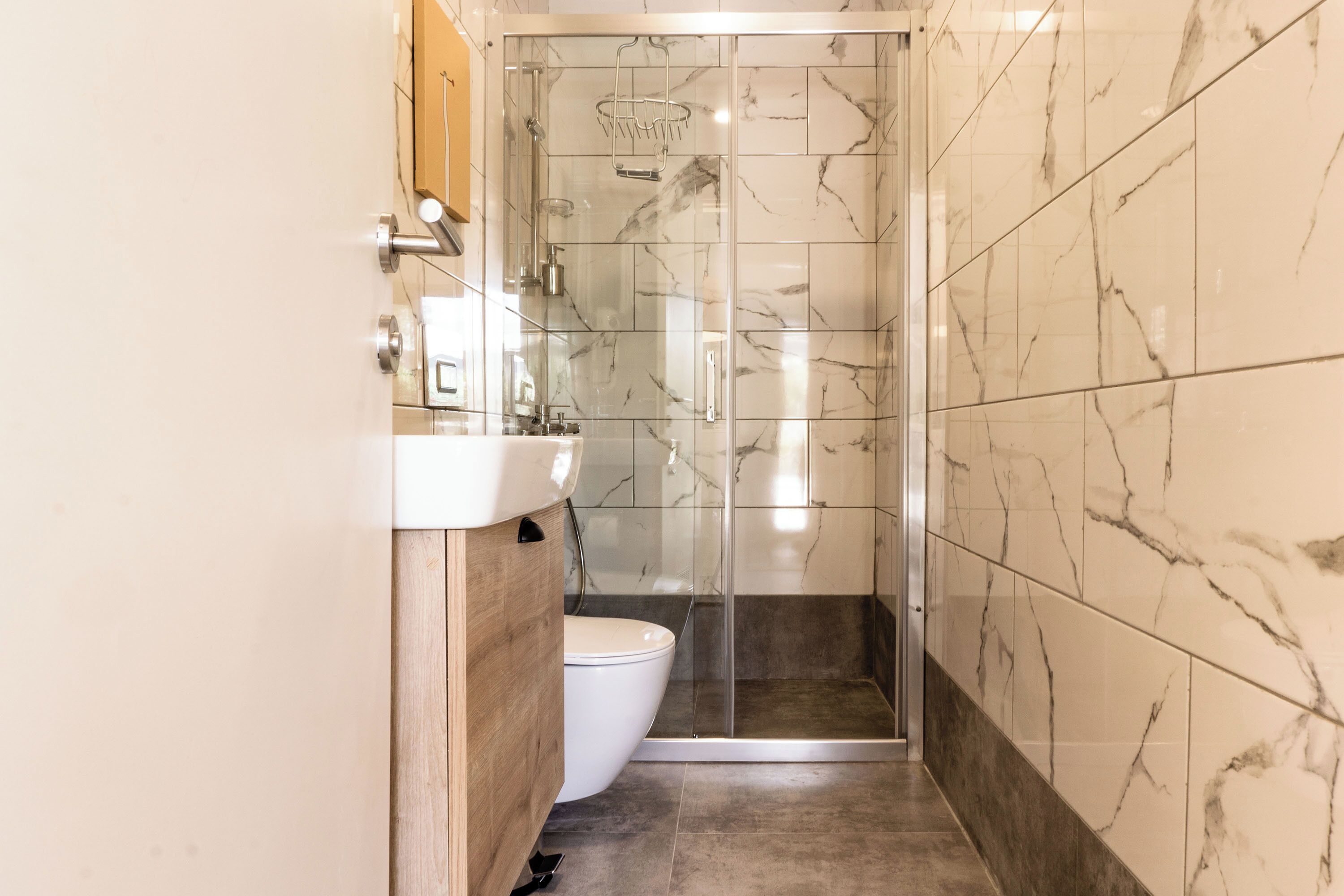 A bathroom with a glass-enclosed shower, a wooden vanity, and a white toilet.