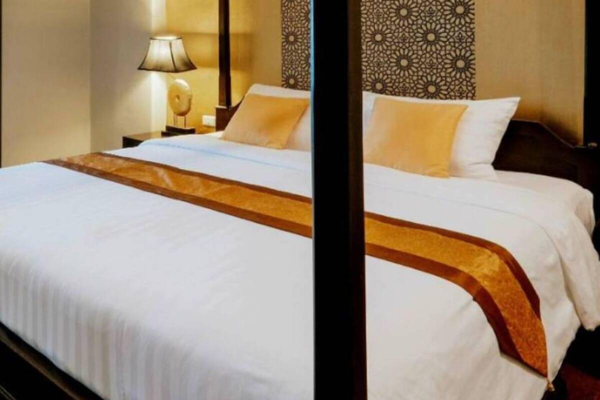 A hotel room with a neatly made bed, a lamp on the nightstand, and a decorative wall panel.