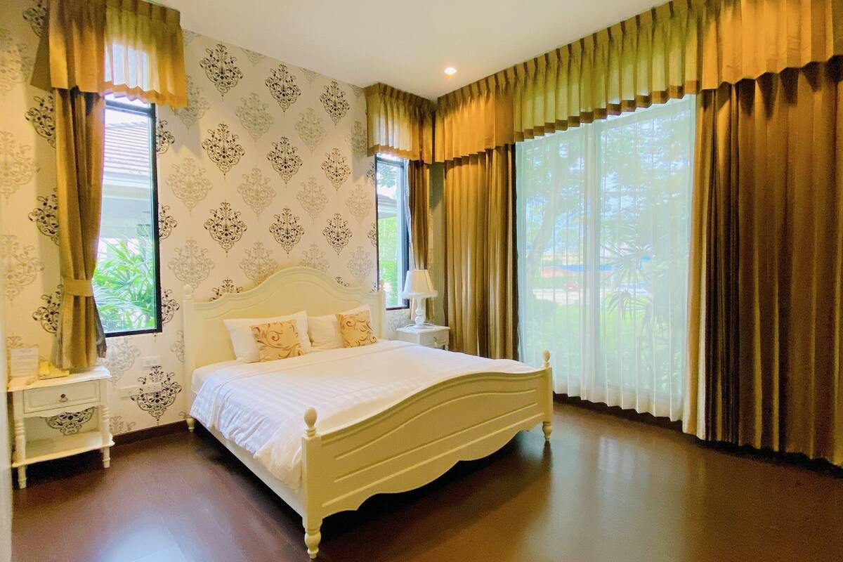 A bedroom with a large bed, two bedside tables, and a window with curtains.