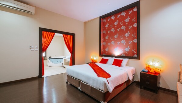 A hotel room with a bed, a nightstand, a wall-mounted lamp, and a bathroom visible through an open door.