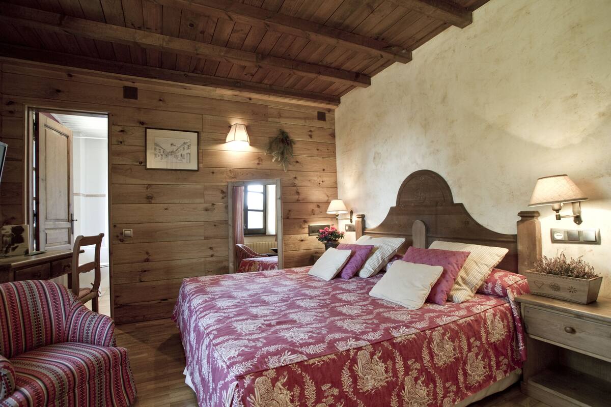 Ein Zimmer mit Holzboden, einem Bett, einem Sessel und einem Schreibtisch.