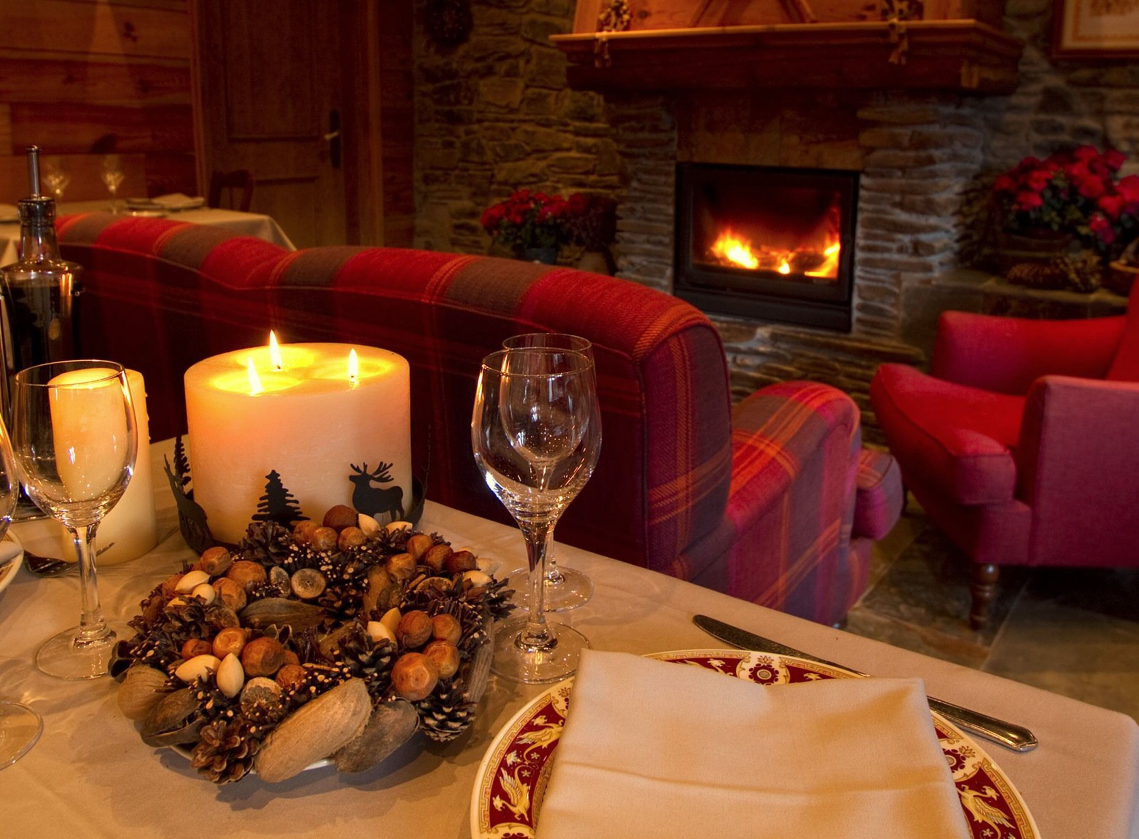 A cozy dining area with a fireplace, a table set with candles, wine glasses, and a decorative centerpiece.