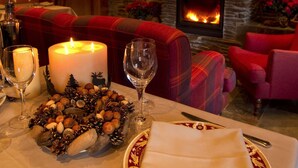 Uma área de jantar aconchegante com lareira, mesa posta com velas, taças de vinho e um centro de mesa decorativo.
