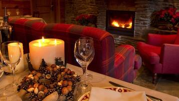 A cozy dining area with a fireplace, a table set with candles, wine glasses, and a decorative centerpiece.