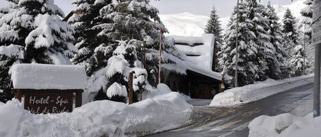 Entrada de hotel coberta de neve, com uma placa indicando 'Hotel - Spa' e 'Val de Puda'.