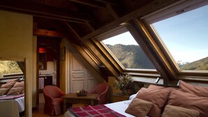 Un dormitorio con una cama grande, una silla roja, un escritorio de madera y vistas a un paisaje montañoso a través de tragaluces.