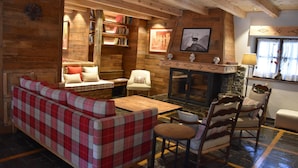 Interior acogedor de una cabaña de madera con chimenea, paredes de madera, un sofá, sillones y una estantería.