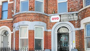 Un immeuble d’angle, avec une enseigne indiquant « OYO Queens Quarter » à l’entrée.