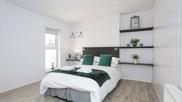Une chambre moderne avec un lit, des tables de chevet, une fenêtre et des étagères intégrées.